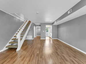 Unfurnished living room featuring stairs, wood finished floors, and baseboards