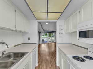 Kitchen featuring white appliances, a sink, white cabinetry, light countertops, and recessed lighting
