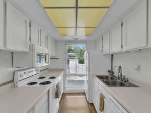 Kitchen featuring white appliances, a sink, white cabinets, and light countertops