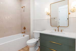 Bathroom with vanity, toilet, wood finished floors, washtub / shower combination, and a wainscoted wall