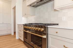 Kitchen featuring double oven range, custom range hood, tasteful backsplash, light wood finished floors, and white cabinets