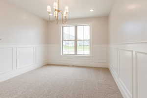 Empty room with a decorative wall, a chandelier, light carpet, a wainscoted wall, and recessed lighting