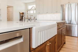 Kitchen with appliances with stainless steel finishes, brown cabinets, light countertops, light wood-style flooring, and a sink