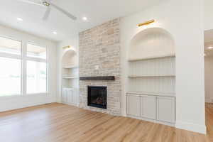 Unfurnished living room featuring ceiling fan, built in features, light wood-style floors, a stone fireplace, and baseboards