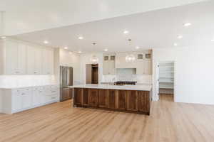 Kitchen featuring high end fridge, light wood-type flooring, backsplash, light countertops, and recessed lighting
