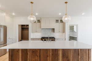 Kitchen featuring high end fridge, a sink, a large island, premium range hood, and backsplash