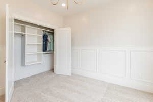 Unfurnished bedroom featuring carpet, a chandelier, a decorative wall, wainscoting, and a closet