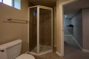 Bathroom featuring toilet, a shower stall, baseboards, and tile patterned flooring