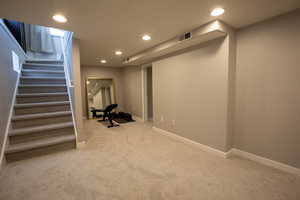 Finished basement featuring light colored carpet, recessed lighting, stairway, and baseboards