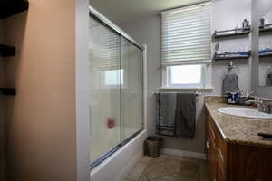 Full bathroom featuring vanity, tile patterned floors, bath / shower combo with glass door, and baseboards