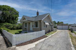Bungalow with a detached garage, an outdoor structure, a chimney, a porch, and a shingled roof
