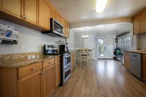 Kitchen with stainless steel appliances, light wood-type flooring, light stone counters, and french doors