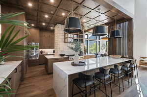 Kitchen featuring coffered ceiling, stainless steel appliances, wood finished floors, decorative backsplash, and light stone countertops