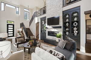 Living room featuring stairway, wood finished floors, a fireplace, baseboards, and a high ceiling