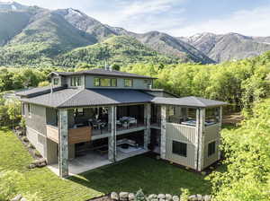 Rear view of property with a patio area, a yard, a mountain view, and roof with shingles