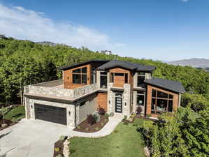 Contemporary house featuring stone siding, a balcony, concrete driveway, a front lawn, and a mountain view