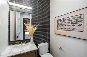 Bathroom featuring tile walls, vanity, toilet, and tasteful backsplash