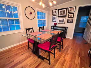 Dining room featuring a chandelier, baseboards, wood finished floors, and ornamental molding
