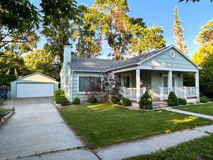 Bungalow-style house featuring a porch, a chimney, a garage, an outdoor structure, and a front yard
