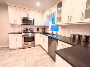 Kitchen featuring stainless steel appliances, a sink, dark countertops, recessed lighting, and backsplash