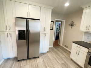 Kitchen featuring stainless steel fridge, baseboards, white cabinetry, light wood-type flooring, and dark countertops