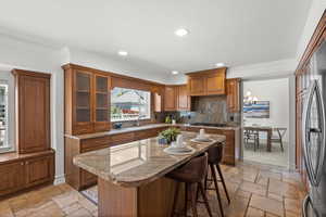 Kitchen featuring stone tile flooring, brown cabinets, a sink, gas stovetop, and recessed lighting.