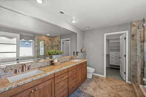 Bathroom with double vanity, a stall shower, toilet, a spacious closet, and baseboards