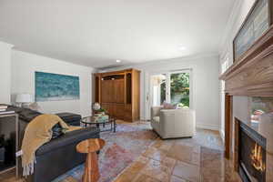 Living room with a fireplace, stone tile flooring, crown molding and recessed lighting.