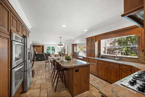 Kitchen with stone tile floors, a sink, appliances with stainless steel finishes, a kitchen island, and recessed lighting.