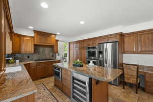 Kitchen with stainless steel appliances, beverage cooler, stone tile floors, ornamental molding, and brown cabinetry.