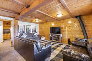 Living area with carpet flooring, wood ceiling with exposed beams, and wood walls