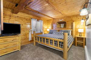Bedroom with a baseboard radiator, wooden ceiling with exposed beams, carpet flooring, and wood walls