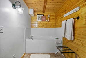 Bathroom featuring wood ceiling with exposed beams, wood walls, a bath, and tile patterned flooring
