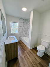 Bathroom with toilet, double vanity, wood finished floors, and wainscoting