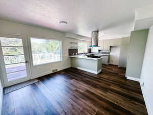 Kitchen featuring island range hood, a peninsula, gas cooktop, dark wood-style flooring, and baseboards