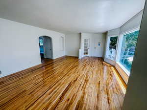 Spare room featuring arched walkways, hardwood / wood-style floors, baseboards, a textured ceiling, and ornamental molding