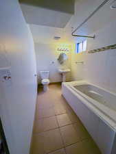 Bathroom featuring toilet, tile patterned floors, a combined bath / shower with jetted tub, baseboards, and a textured ceiling