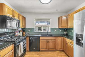 Kitchen with black appliances, a sink, light wood-style floors, and brown cabinetry
