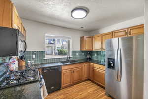 Kitchen featuring black appliances, a sink, light wood-style flooring, and backsplash