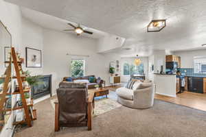 Living room featuring light carpet, ceiling fan, a glass covered fireplace, and a textured ceiling