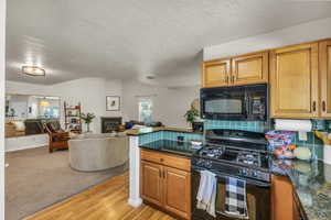 Kitchen with black appliances, open floor plan, light wood-style flooring, brown cabinetry, and a textured ceiling