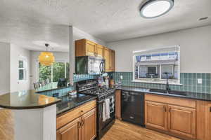 Kitchen with black appliances, a sink, light wood-style floors, brown cabinets, and a peninsula