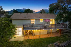 Back of property at dusk featuring a patio, a deck with mountain view, a yard, and roof with shingles