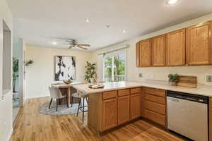 Kitchen featuring light countertops, a peninsula, stainless steel dishwasher, light wood-style floors, and brown cabinets