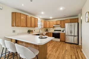 Kitchen featuring a peninsula, freestanding refrigerator, light countertops, white range with electric cooktop, and brown cabinets