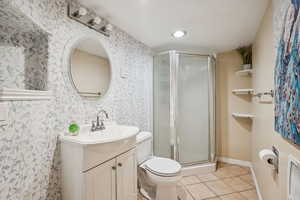 Full bathroom with vanity, a shower stall, tile patterned floors, wallpapered walls, and toilet