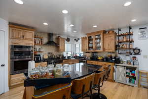 Kitchen featuring open shelves, wall chimney range hood, stainless steel double oven, decorative backsplash, and brown cabinetry