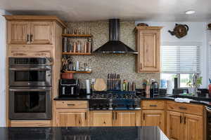 Kitchen with wall chimney range hood, double oven, gas cooktop, tasteful backsplash, and a textured ceiling