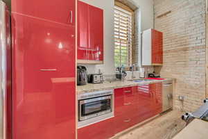 Kitchen with light wood-style floors, brick wall, red cabinetry, appliances with stainless steel finishes, and a sink