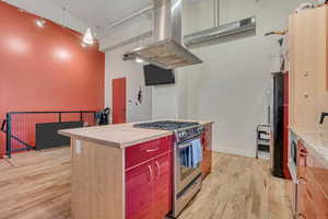 Kitchen featuring stainless steel range with gas stovetop, island exhaust hood, light wood finished floors, a high ceiling, and freestanding refrigerator
